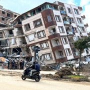 A person on a motorbike drives past a collapsed building