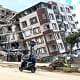 A person on a motorbike drives past a collapsed building